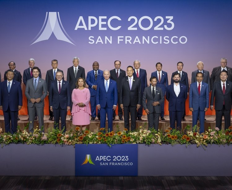 A large group of world leaders stand on a stage in front of a logo for APEC 2023.
