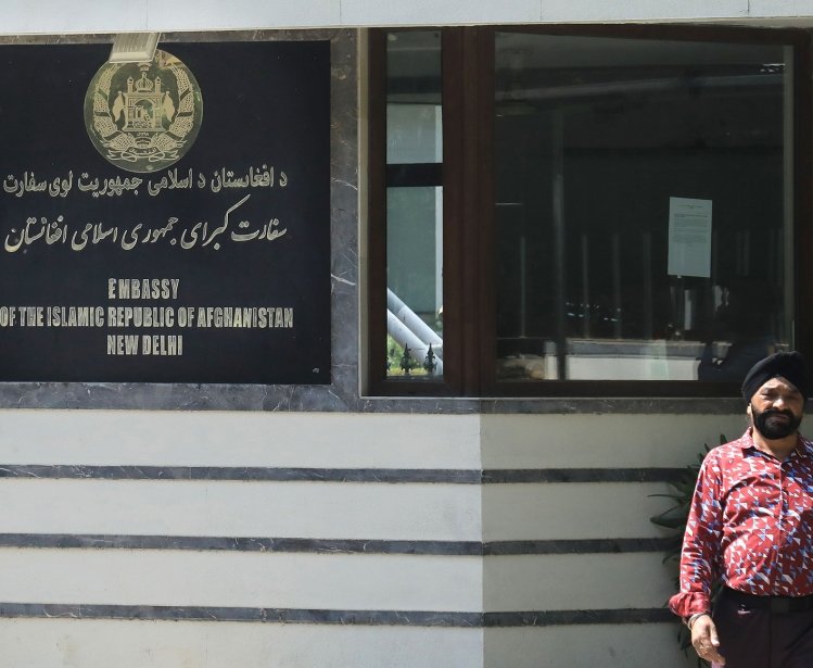 A man stands outside a building with a sign that reads Embassy of the Isalamic Republic of Afghanistan, New Delhi