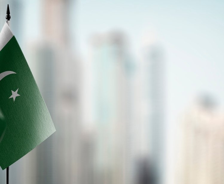 Two small Pakistani flags on a table with an out of focus city skyline in the background.