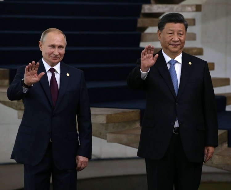 Russian President Vladimir Putin and Chinese President Xi Jinping wave while standing next to each other