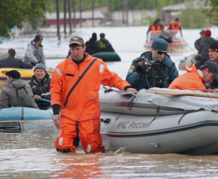 Man walking in knee-high water pulling a raft with people in it