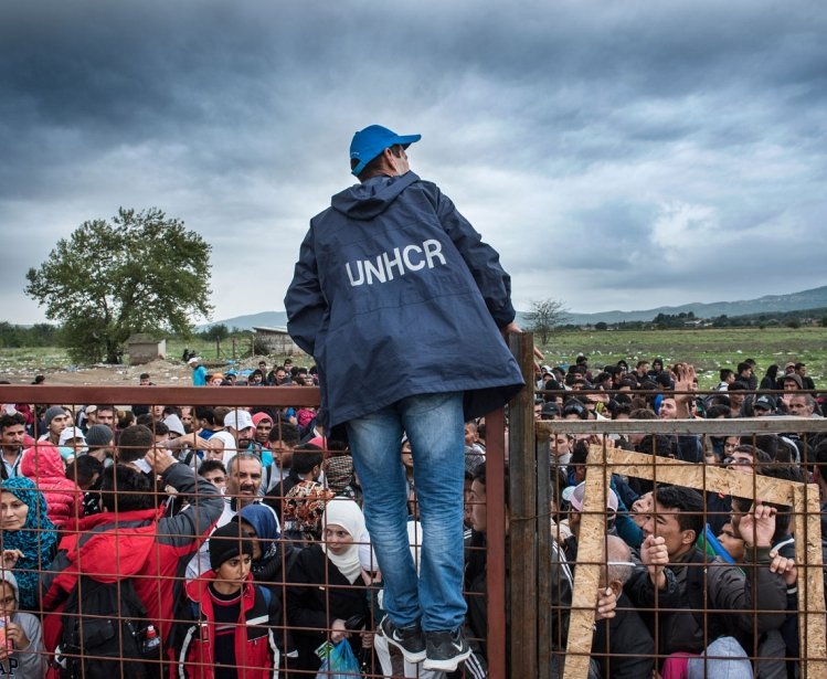 Gevjelija, Macedonia - September 26, 2015. A UNHCR employee talks to refugees as they wait during a rainstorm to enter inside a refugee camp near the town of Gevgelija at the Macedonian - Greek border
