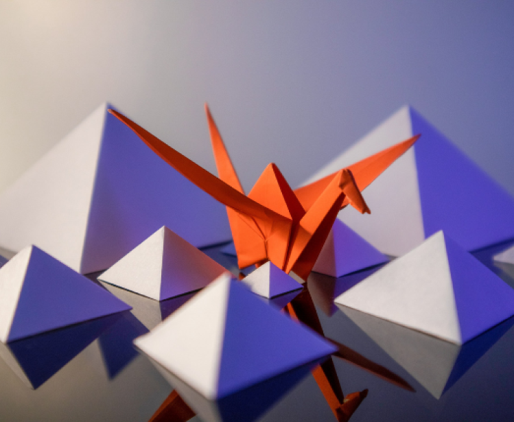 Abstract origami pyramids and a crane sit on a reflective surface.
