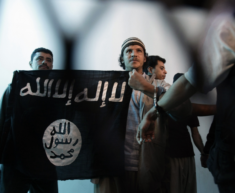 n this April 23, 2013 file photo, a suspected Yemeni al-Qaida militant, center, holds a banner as he stands behind bars during a court hearing in state security court in Sanaa, Yemen