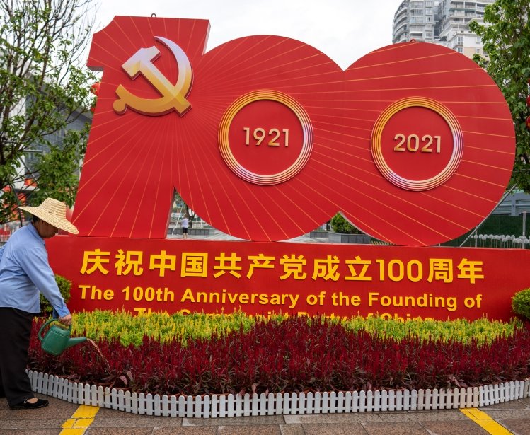 A gardener waters plants in front of a CCP at 100th installation 