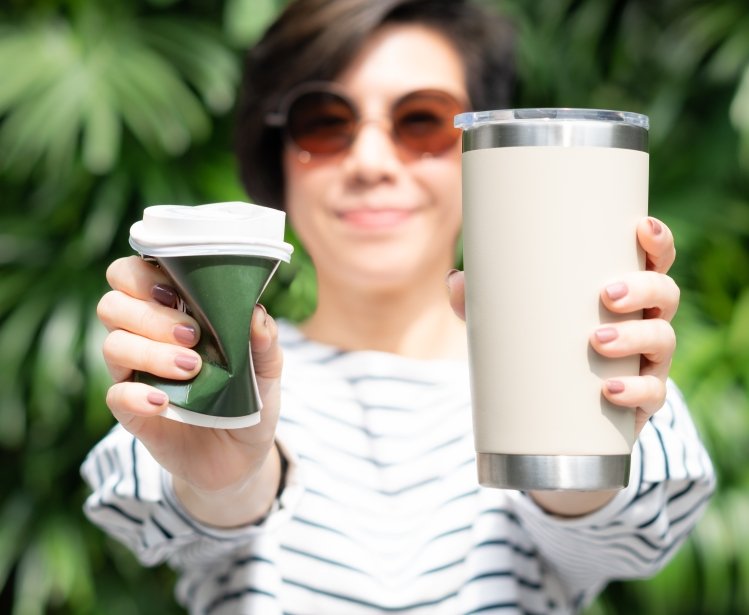 a woman holding one single-use cup and one reusable mug