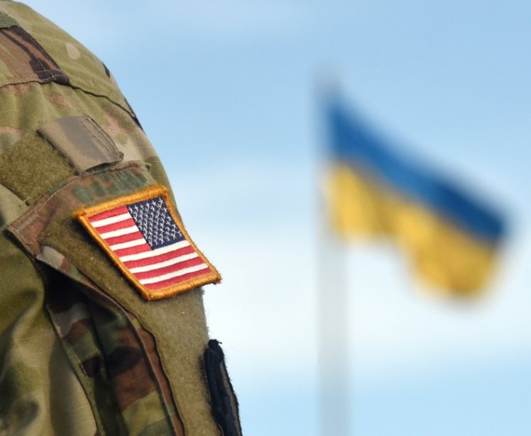 American soldier stands in front of the Ukrainian flag