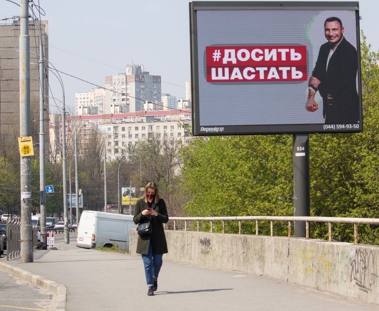 April 17 2020: Girl in a mask on a city street and a banner with the image of the mayor of Kyiv, sign reading "Do not go" in the Ukrainian language