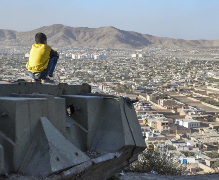 A boy sits on a ledge overlooking Kabul