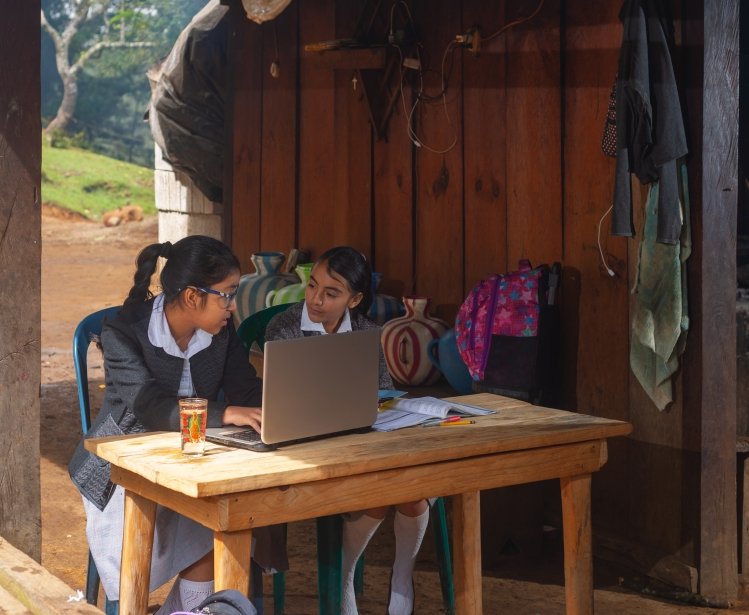 Two girls sitting in front of a computer in the rural outdoors.