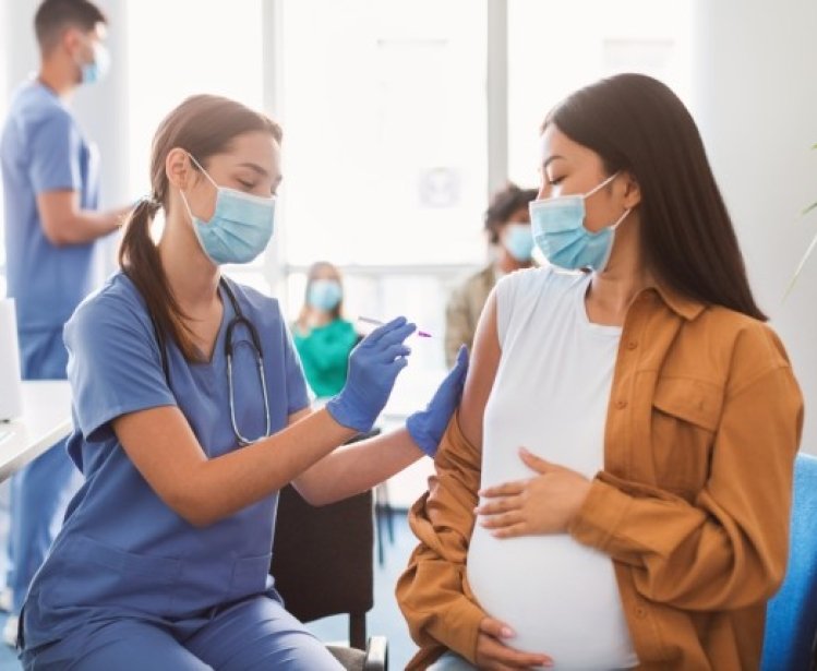 Pregnant woman wearing a mask and receiving a vaccine from a provider in scrubs wearing a mask