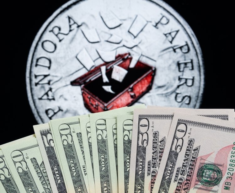 Money and blurred Pandora Papers token, symbol of leaked documents seen on the screen behind. Concept. Stafford, United Kingdom, October 5, 2021.