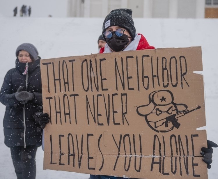 Protester in snow with sign that reads "That one neighbor that never leaves you alone" and a caricature representing the Russian state