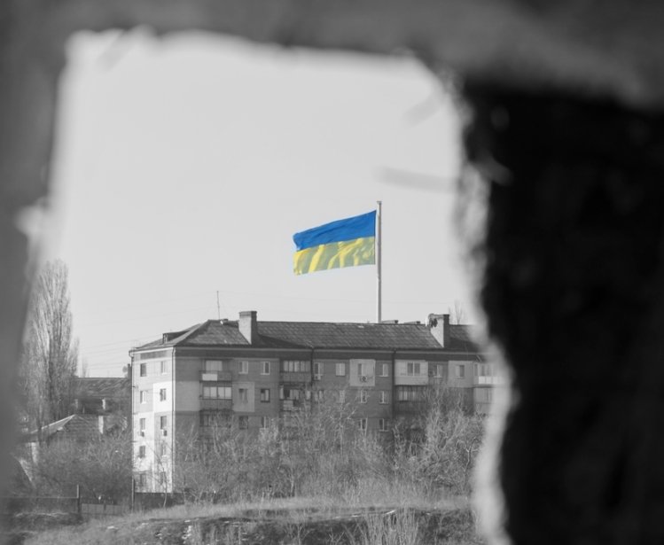 View through the window of the ruined house on the flag of Ukraine in the blue sky. Russia's aggression against Ukraine. The concept of peace after the war.f