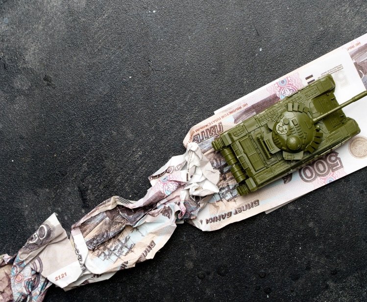 A toy tank runs over Russian ruble notes