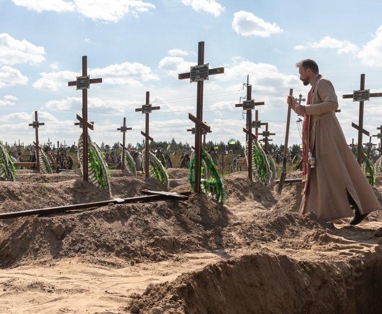 A priest overseas the burial of the remains of 13 unidentified and two identified people who were killed in the Bucha district during the Russian occupation