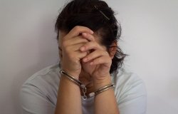 A woman in handcuffs hides her face behind her hands.