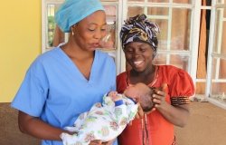 Two women, one in blue scrubs holding a baby