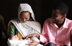 Nefisa, a farmer who lives in the Oromia Region of Ethiopia, smiling with her husband and healthy child