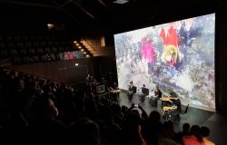 Audience watching a musical performance with abstract image in background of stage
