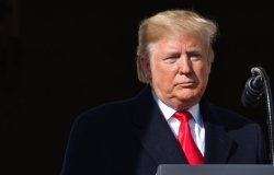 Donald Trump stands silently at a microphone, part of his face in shadow