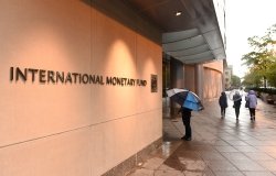 People with umbrellas walking past a building with a sign that says International Monetary Fund.