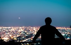 A man looking out at a city skyline at night.