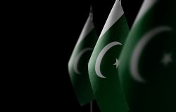 Three Pakistan flags fade from view into a dark background