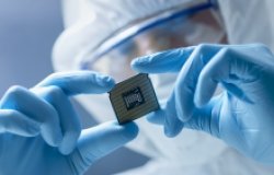 A person in a clean suit holding up a computer chip