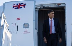 Prime Minister Rishi Sunak exits a plane with a UK flag visible on the door.
