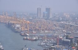 An aerial view of a port with cranes, ships, and skyscrapers.