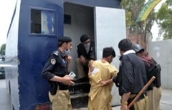 Police officials are pushing a man with torn clothing into the back of a police vehicle after he has been arrested.