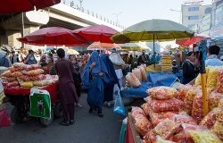 Afghan men and women in traditional clothing shop at an outdoor market.