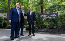 Presidents Yoon and Biden stand with Prime Minister Kishida in front of the sign for Camp David.