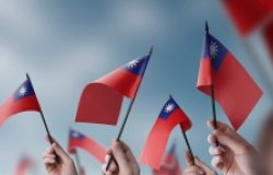 A close up of hands waving small Taiwanese flags.