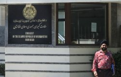 A man stands outside a building with a sign that reads Embassy of the Isalamic Republic of Afghanistan, New Delhi