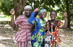 Group of young African villagers in colorful traditional dresses smiling at the camera. 