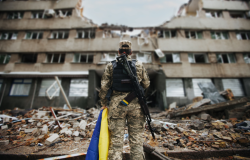 Ukrainian soldier stands with Ukrainian flag in front of destroyed apartment complex
