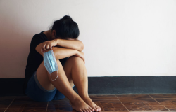 Girl sits on the floor with her head in arms, holding a mask.