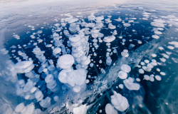 Gas methane bubbles frozen in winter ice of lake Baikal, abstract background.