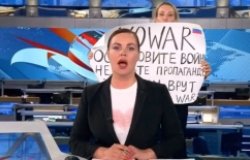 A protester holding sign behind a newscaster 