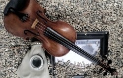 Image of a gas mask, violin and framed photo in gravel