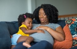 African American little girl holding her mother’s stomach.