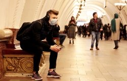 A young man with a backpack sits at a Moscow metro station with a medical mask