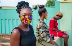 Three African women sitting apart, observing social distance - woman wearing made home made mask and looking at camera