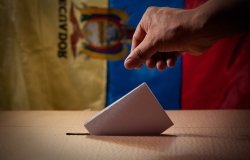 Hand casting a ballot in front of an Ecuadorian flag