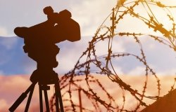 A composite photo with the Russian flag in the background, and barbed wire and a television news camera in the foreground