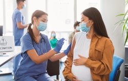 Pregnant woman wearing a mask and receiving a vaccine from a provider in scrubs wearing a mask