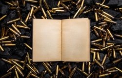 open book in a black hardcover with yellowed blank pages. Empty gun cases lying on charred coals.