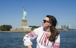 Woman in traditional Ukrainian dress sitting in front of the statue of Liberty